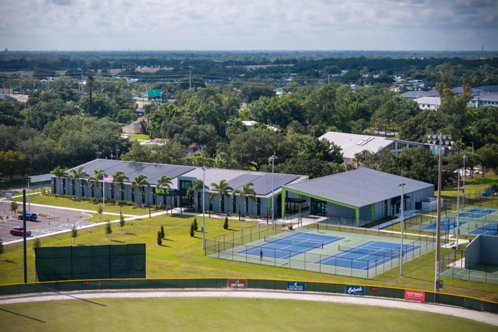 Elevated view of the Twin Lakes Park campus with the solar-roofed Administration and Multi-Purpose buildings beside tennis and pickleball courts and a ball field.